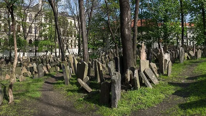 Tombes anciennes inclinées et serrées les unes contre les autres dans le vieux cimetière juif de Prague, au milieu des arbres.