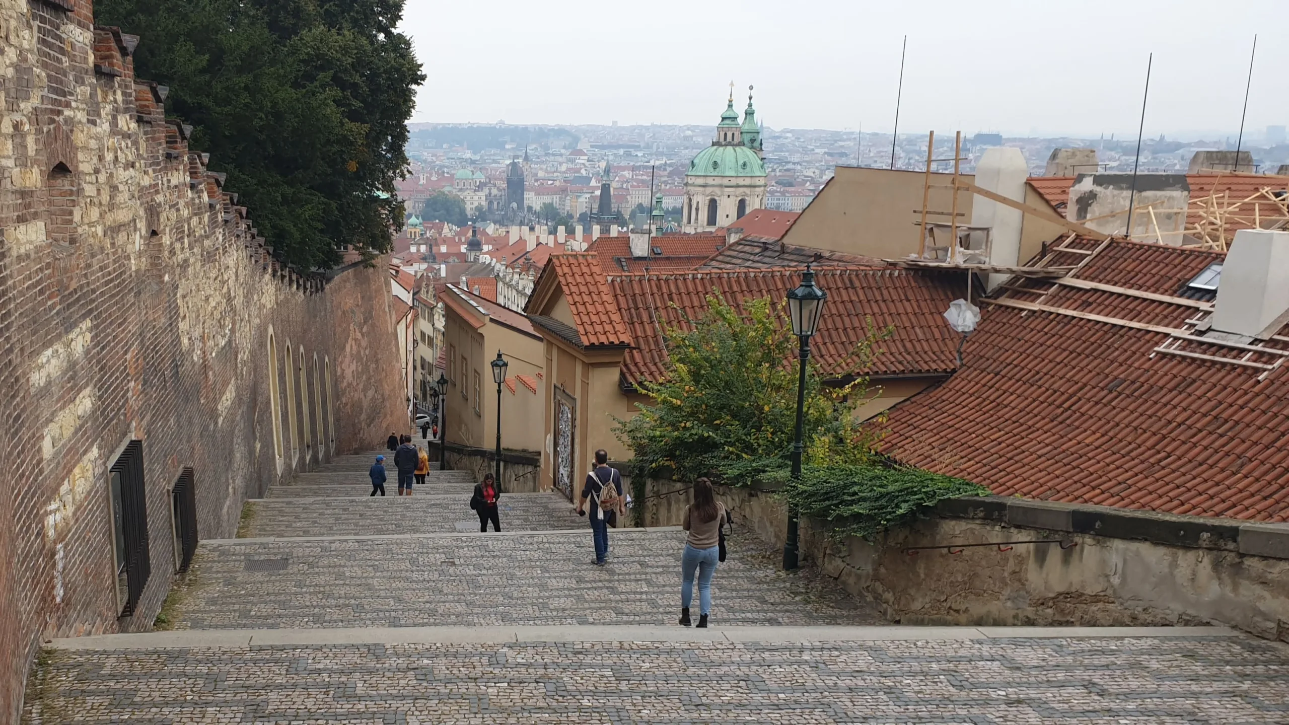 Escaliers pavés descendant du château de Prague vers Malá Strana, avec les toits rouges de la ville et le dôme de l'église Saint-Nicolas.