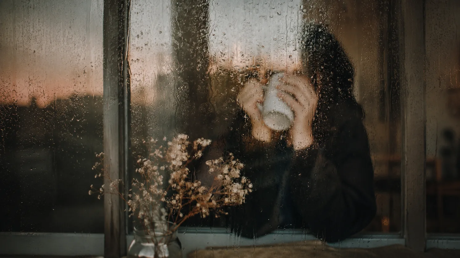 Personne buvant un café derrière une vitre couverte de pluie